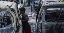 Seorang anak kecil melihat kendaraan roda empat yang terbakar saat demonstrasi di Mako Brimob Polda Metro Jaya, Kwitang, Jakarta Pusat, Jumat, 29 Agustus 2025. (Sumber: Poskota/Bilal Nugraha Ginanjar)
