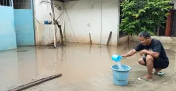 Himin, 52 tahun, Warga Kampung Lebak, Teluk Pucung, Kota Bekasi, berusaha membuang genangan air yang ada di luar rumahnya akibat banjir kiriman dari Bogor, Senin, 7 Juli 2025. (Sumber: Poskota/Nurpini Aulia Rapika)