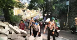 Petugas Lantas Polsek Bojongsati dibantu warga dan Dishub membersihkan puing-puing batu hebel yang tumpah dari truk terguling di Jalan Raya Muchtar, Sawangan, Kota Depok, Rabu pagi, 16 Juli 2025. (Sumber: Poskota/Angga Pahlevi)
