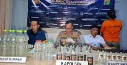 Kapolsek Bojongsari Kompol Fauzan bersama Kanit Reskrim Iptu Sugeng memperlihatkan barang bukti miras oplosan dan pelaku sebagai pemilik warung jamu. (Sumber: Poskota/Angga Pahlevi)