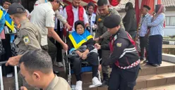 Petugas haji dan Satpol PP membantu jemaah haji lanjut usia menuruni tangga Gedung Tegar Beriman, Cibinong saat pelepasan kloter pertama Kabupaten Bogor, Kamis 23 April 2026. (Sumber: Poskota/Giffar Rivana)