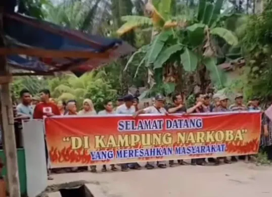 Spanduk kontroversial bertuliskan ‘Selamat Datang di Kampung Narkoba’ terpampang di Dusun Balam Timur, sebagai bentuk protes warga terhadap peredaran narkoba yang tidak kunjung ditangani.