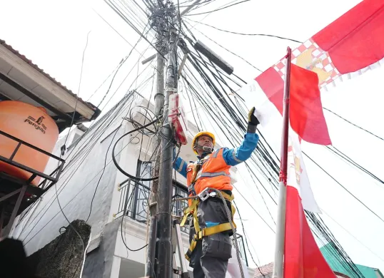 Petugas PLN sedang merapikan bendera dekorasi 17an yang menempel dengan jaringan listrik. Pemasangan seperti ini berisiko tinggi dan tidak aman. (Sumber: Dok. PLN UID Jakarta Raya)