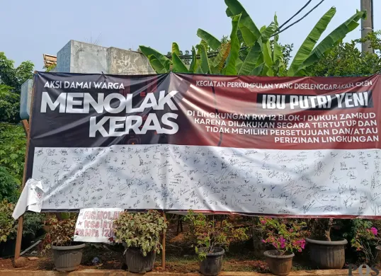 Spanduk petisi penolakan kegiatan keagamaan Umi Cinta yang diduga menyimpang oleh warga Perumahan Dukuh Zamrud, Mustikajaya, Kota Bekasi terbentang lebar di depan rumah Umi Cinta. (Sumber: POSKOTA | Foto: Nurpini Aulia Rapika)