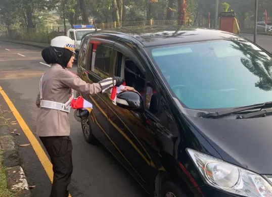 Kanit Kamsel Satlantas Polres Metro Depok AKP Elly Padiansari membagikan bendera merah putih sekaligus menyapa pengendara motor dan mobil untuk menyemarakkan HUT Kemerdekaan RI ke-80 di Lingkar Fly Over UI, Kota Depok. (Sumber: Poskota/Angga Pahlevi)