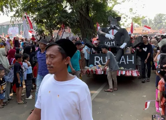 Peserta karnaval 17 Agustus 2025 di Kecamatan Menes, Pandeglang, membawa ornamen tikus berdasi ukuran besar. (Sumber: POSKOTA | Foto: Samsul Fatoni)