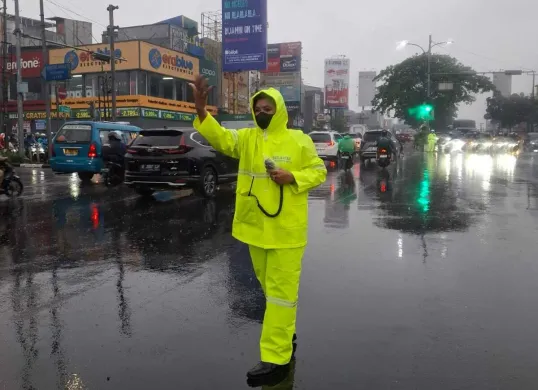 Kanit Turjawali Satlantas Polres Metro Depok, AKP Fitri (mengenakan jas hujan) mengatur lalu lintas di Jalan Margonda, saat hujan deras yang menyebabkan kemacetan, Selasa, 19 Agustus 2025. (Sumber: Poskota/Angga Pahlevi)
