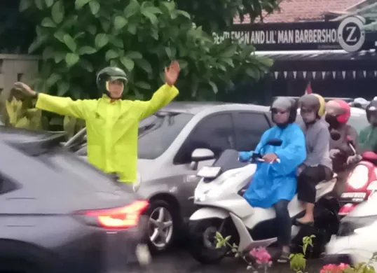 Seorang polisi mengenakan jas hujan mengatur arus lalu lintas di Jalan Raya Cinere, Depok, saat hujan deras yang menyebabkan kemacetan pada Selasa, 19 Agustus 2025). (Sumber: Poskota/Angga Pahlevi)