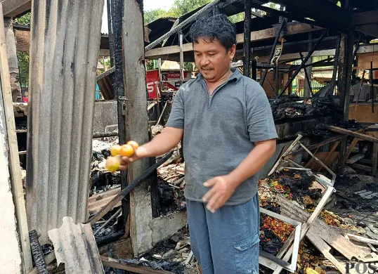Asep, salah satu pedagang Pasar Pejuang Pratama, mengais buah jeruk miliknya yang tersisa di antara puing dan arang bekas kebakaran, Minggu 24 Agustus 2025. (Sumber: POSKOTA | Foto: Nurpini Aulia Rapika)