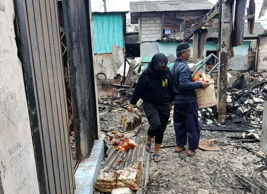Pedagang Pasar Pejuang Pratama mengais sisa dagangan yang masih bisa diselamatkan usai kios mereka ludes terbakar, Sabtu malam, 23 Agustus 2025. (Sumber: POSKOTA | Foto: Nurpini Aulia Rapika)