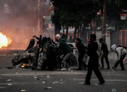 Massa aksi berlindung di balik tameng saat bentrok dengan pihak keamanan di Satuan Brimob Polda Metro Jaya, Kecamatan Senen, Jakarta Pusat, Jumat, 29 Agustus 2025. (Sumber: Poskota/Bilal Nugraha Ginanjar)
