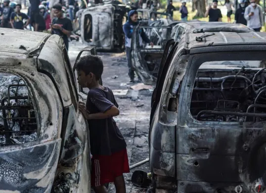 Seorang anak kecil melihat kendaraan roda empat yang terbakar saat demonstrasi di Mako Brimob Polda Metro Jaya, Kwitang, Jakarta Pusat, Jumat, 29 Agustus 2025. (Sumber: Poskota/Bilal Nugraha Ginanjar)