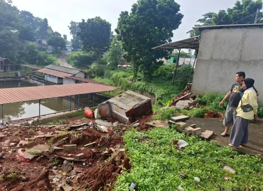 Warga melihat kondisi tebing pembatas Perumahan SIK di Kelurahan Kedaung, Sawangan, Depok, yang longsor akibat luapan air Setu Tujuh Muara setelah hujan deras, Kamis, 11 Desember 2025. (Sumber: Poskota/Angga Pahlevi)