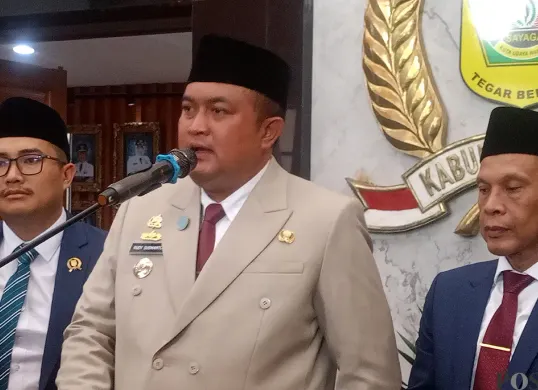 Bupati Bogor, Rudy Susmanto (tengah), menyampaikan keterangan kepada awak media seusai Rapat Paripurna di Gedung DPRD, Selasa, 16 Desember 2025. (Sumber: POSKOTA | Foto: Giffar Rivana)