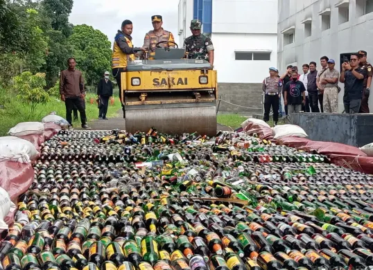 Kapolres Cimahi, AKBP Niko N Adi Putra (tengah), menggilas ribuan botol minuman beralkohol menggunakan alat berat, di Lapangan BPKB Mapolres Cimahi, Jumat 19 Desember 2025. (Sumber: Poskota | Foto: Gatot Poedji Utomo)