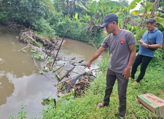 Ketua RT 2/01 Desa Nanggerang, Kecamatan Tajurhalang, Wawih bersama anggota Opsnal Kecamatan Tajurhalang mengecek lokasi penemuan jasad bayi di Kali Caringin, Sabtu 8 Februari 2025. (Sumber: Poskota/Angga Pahlevi)