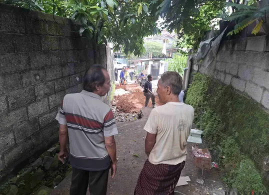 Heri (kanan) bersama warga sedang melihat jalan yang amblas di lingkungan mereka sedang diperbaiki oleh Dinas PUPR Kota Depok, Jumat siang, 14 Februari 2025. (Sumber: Poskota/Angga Pahlevi)