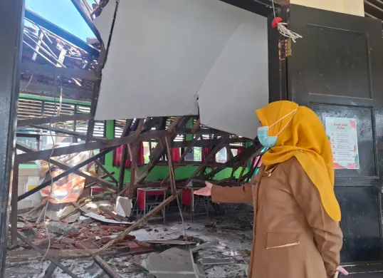 Kepala Sekolah SDN Mekarjaya 29 Kota Depok, Rika Kartini, menunjukkan ambruknya atap ruang kelas di SDN tersebut, karena rangka kayu yang sudah lapuk termakan usia, Senin, 13 Januari 2025. (Sumber: Poskota/Angga)