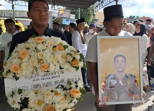 Kedua adik korban Raihan dan Viko saat memegang karangan bunga dan foto dinas almarhum Iqbal Anwar Arif, di Bekasi Selatan, Kota Bekasi. Minggu, 19 Desember 2025. (Sumber: Poskota/Ihsan Fahmi)