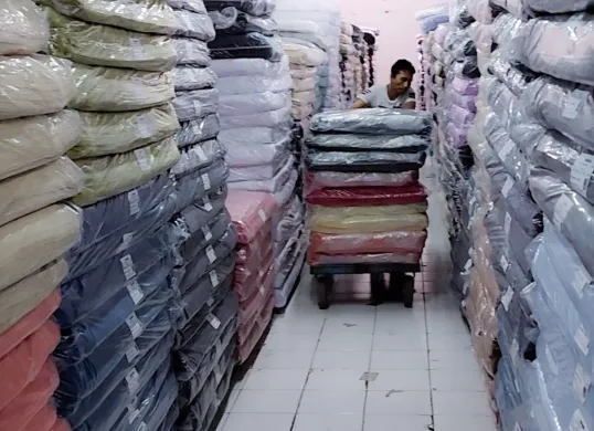 Pekerja Focus Textile mendorong tumpukan kain yang dikemas rapi di salah satu gudang. Industri tekstil tetap beroperasi di tengah tekanan ekonomi dan persaingan impor. (Sumber: Istimewa)