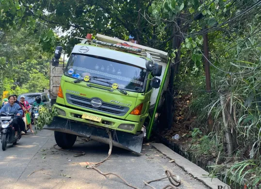 Truk Hino berwarna hijau-putih terperosok ke parit setelah gagal menanjak di Tanjakan Parakan, Pamulang, Tangerang Selatan, pada Jumat, 4 Juli 2025. (Sumber: Poskota/Primayanti Juli Kumala Manalu)