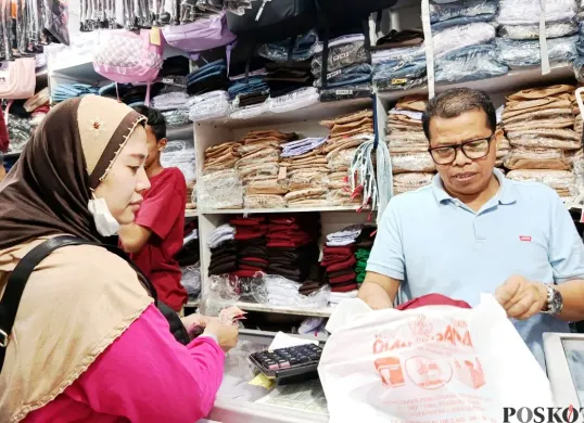 Anies, 54 Tahun, pemilik toko seragam sekolah sedang melayani pelanggan di Pasar Baru Bekasi, Minggu, 13 Juli 2025. (Sumber: Poskota/Nurpini Aulia Rapika)