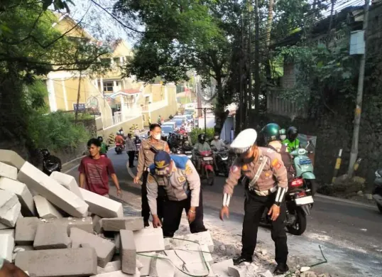 Petugas Lantas Polsek Bojongsati dibantu warga dan Dishub membersihkan puing-puing batu hebel yang tumpah dari truk terguling di Jalan Raya Muchtar, Sawangan, Kota Depok, Rabu pagi, 16 Juli 2025. (Sumber: Poskota/Angga Pahlevi)