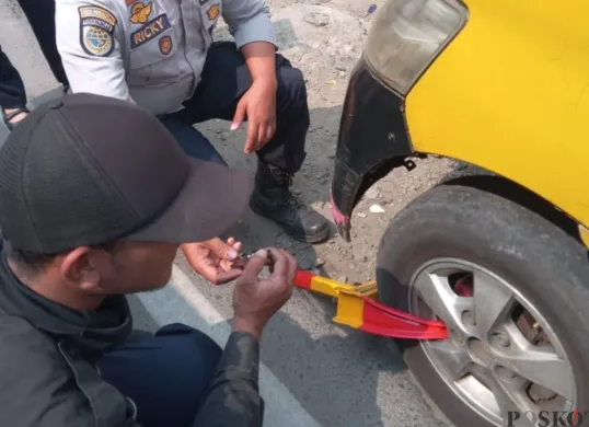 Petugas mengunci ban mobil dalam penertiban di kawasan Padalarang, Kabupaten Bandung Barat, Rabu, 23 Juli 2025. (Sumber: Poskota/Gatot Poedji Utomo)