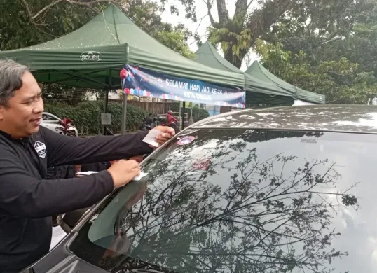 Petugas DLH Kota Cimahi memasang stiker tanda lolos uji emisi pada kendaraan. (Sumber: POSKOTA | Foto: Gatot Poedji Utomo)
