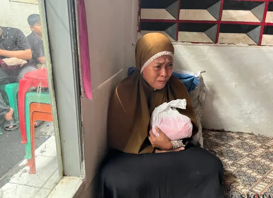 Nurjanah, 49 tahun, orangtua korban kebakaran rumah tinggal di Tebet, Jaksel, sedang menggendog buntelan plastik berisikan bagian tubuh anaknya yang terbakar, Kamis, 19 Juni 2025. (Sumber: Poskota/Pandi Ramedhan)