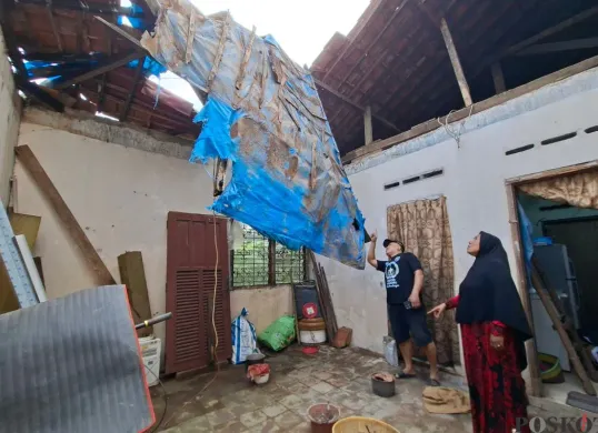 Oma Endah didampingi Ketua RT menujukkan atap yang ambruk tidak tersisa hanya ada sisa terpal untuk menahan air dari banjir di Kota Depok, Jumat, 20 Juni 2025. (Sumber: Poskota/Angga Pahlevi)