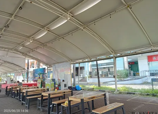 Suasana di area kuliner untuk UMKM yang berlokasi di luar sebuah pusat perbelanjaan, Grand Mall Bekasi. Deretan meja dan bangku kayu terlihat kosong, menanti kedatangan pengunjung di bawah naungan tenda. (Sumber: Poskota/Nurpini Aulia Rapika)