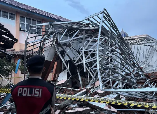 Petugas polisi berjaga di SMKN 1 Gunung Putri yang ambruk akibat hujan deras dan angin kencang yang melanda wilayah tersebut. (Sumber: POSKOTA | Foto: Giffar Rivana)