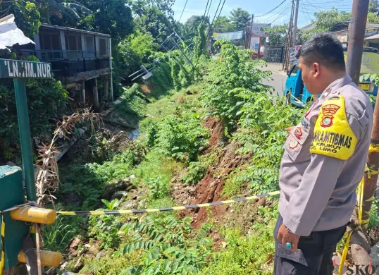 Petugas kepolisian menunjukan tebing longsor di Jalan Raya Krukut RT 04/RW 01, Kelurahan Krukut. Kecamatan Limo, Kota Depok, Selasa, 4 November 2025. (Sumber: Poskota/Angga Pahlevi)