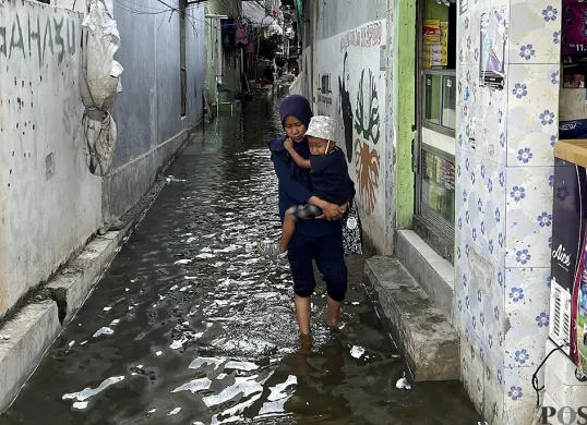 Warga melintasi genangan air akibat banjir rob di RW 22 Kelurahan Muara Angke, Kecamatan Penjaringan, Jakarta Utara pada Sabtu, 22 November 2025. (Sumber: POSKOTA | Foto: Pandi Ramedhan)