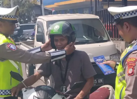 Kanit Lantas Polsek Cinere, Iptu Suharyoko memasangkan helm kepada pengendara saat Operasi Zebra Jaya 2025. (Sumber: Dok. Polsek Cinere)