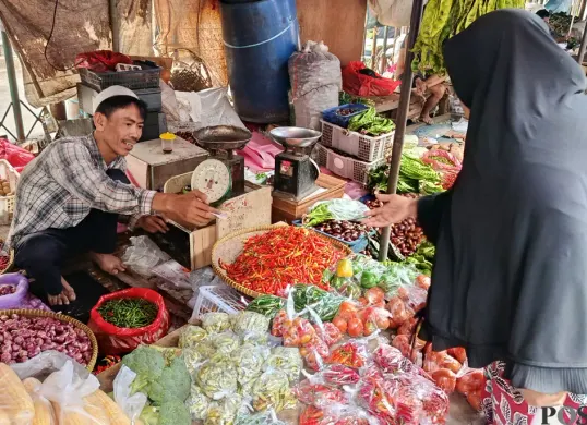 Hasanudin, pedagang sayur di Pasar Baru Bekasi Timur sedang melayani pembeli di lapaknya, Selasa, 7 Oktober 2025. (Sumber: POSKOTA | Foto: Nurpini Aulia Rapika)