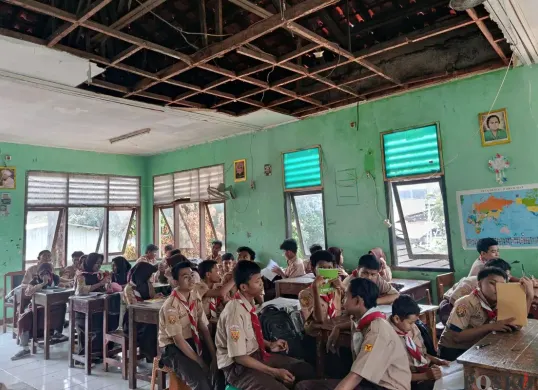 Suasana sejumlah siswa USB SMPN 62 Kota Bekasi mengikuti kegiatan belajar mengajar di ruang kelas dengan atap nyaris roboh, Rabu, 8 Oktober 2025. (Sumber: Poskota/Nurpini Aulia Rapika)