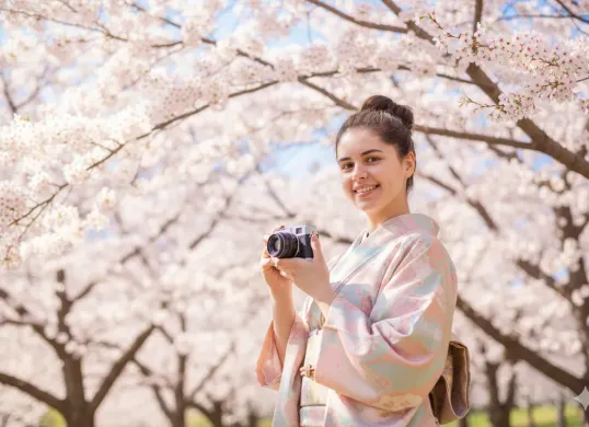 Hasil edit prompt Gemini AI terbaru edit foto wanita liburan di Jepang dengan view bunga sakura. (Sumber: Freepik/user18526052)
