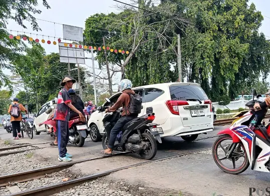 Suasana pelintasan kereta Bulak Kapal, Bekasi Timur, tanpa palang pintu di kedua sisinya. Petugas bersama warga mengatur lalu lintas yang padat, Minggu 14 September 2025. (Sumber: POSKOTA | Foto: Nurpini Aulia Rapika)