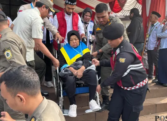 Petugas haji dan Satpol PP membantu jemaah haji lanjut usia menuruni tangga Gedung Tegar Beriman, Cibinong saat pelepasan kloter pertama Kabupaten Bogor, Kamis 23 April 2026. (Sumber: Poskota/Giffar Rivana)