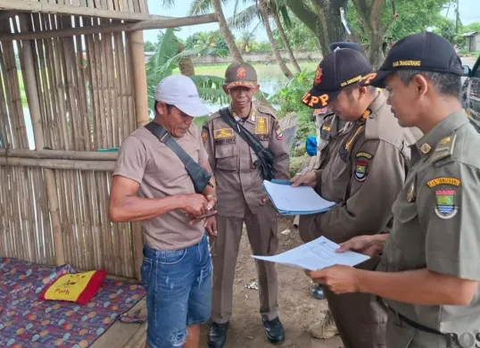 Anggota Satpol PP Kabupaten Tangerang mengirimkan surat peringatan kepada pemilik bangunan liar di Jalan Raya Pakuhaji, Desa Keramat, Kecamatan Pakuhaji, Kabupaten Tangerang. (Sumber: Poskota/Veronica Prasetio)