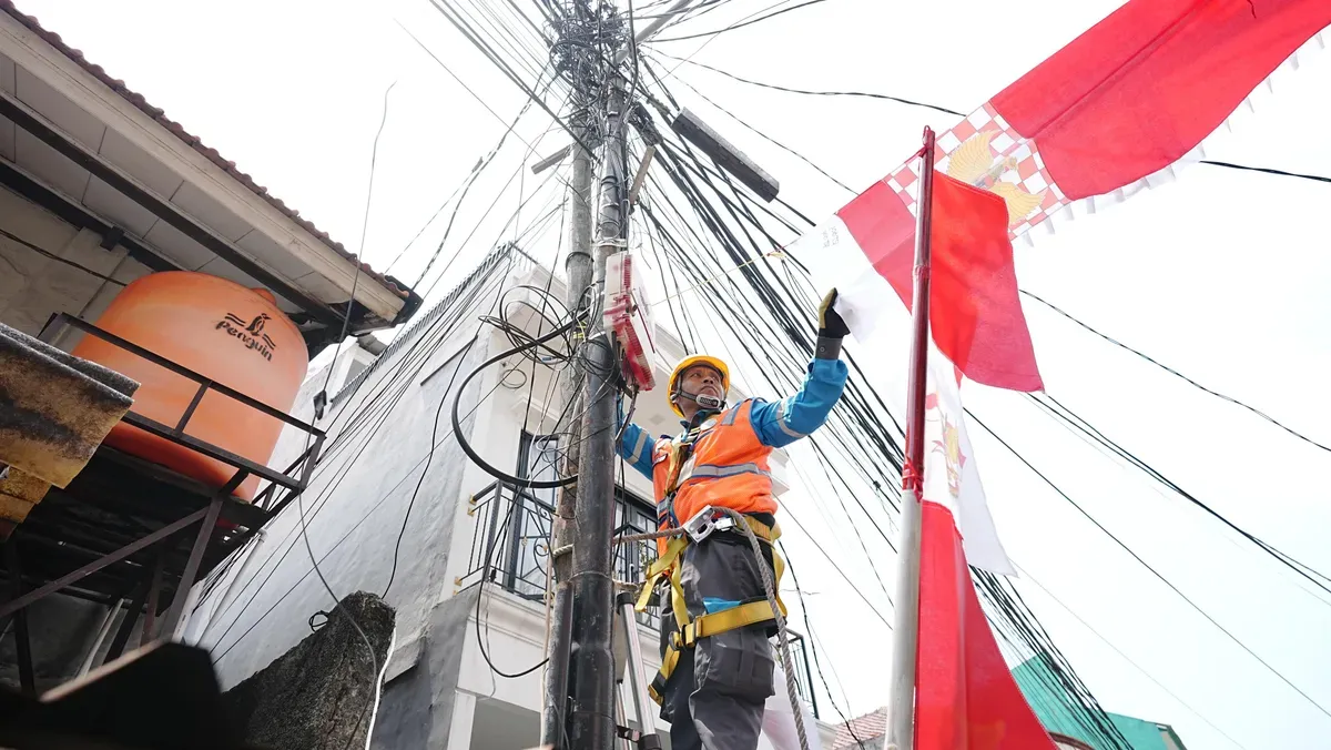 Petugas PLN sedang merapikan bendera dekorasi 17an yang menempel dengan jaringan listrik. Pemasangan seperti ini berisiko tinggi dan tidak aman. (Sumber: Dok. PLN UID Jakarta Raya)