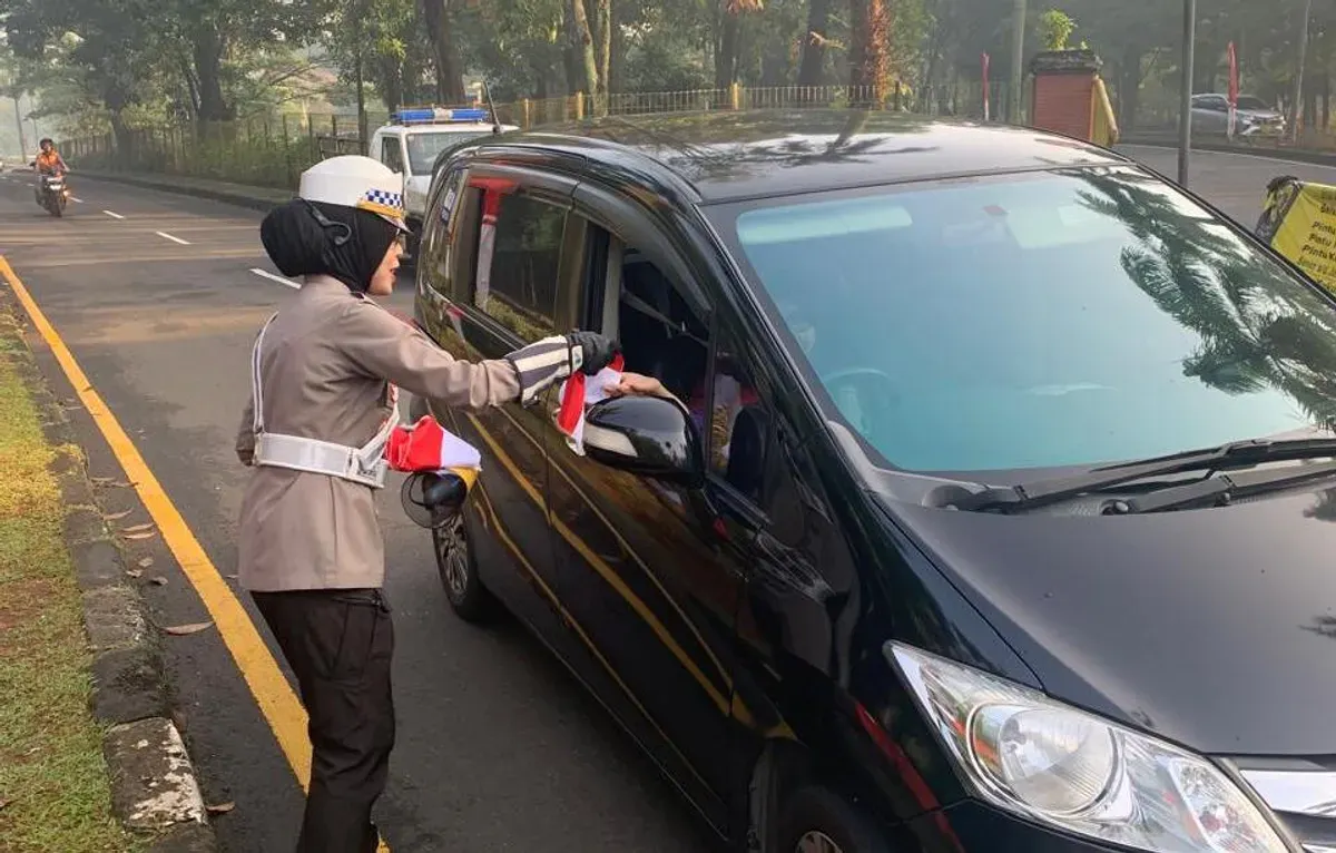 Kanit Kamsel Satlantas Polres Metro Depok AKP Elly Padiansari membagikan bendera merah putih sekaligus menyapa pengendara motor dan mobil untuk menyemarakkan HUT Kemerdekaan RI ke-80 di Lingkar Fly Over UI, Kota Depok. (Sumber: Poskota/Angga Pahlevi)