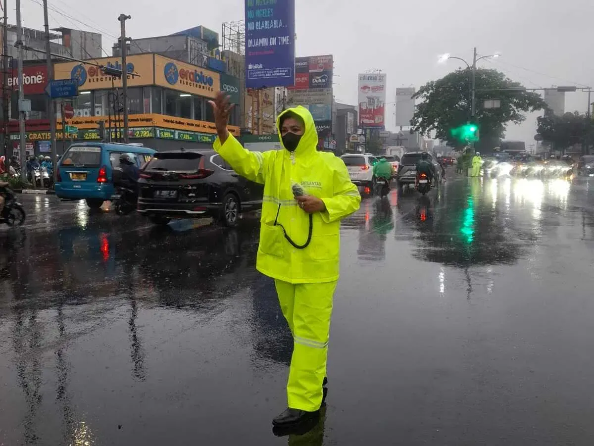 Kanit Turjawali Satlantas Polres Metro Depok, AKP Fitri (mengenakan jas hujan) mengatur lalu lintas di Jalan Margonda, saat hujan deras yang menyebabkan kemacetan, Selasa, 19 Agustus 2025. (Sumber: Poskota/Angga Pahlevi)