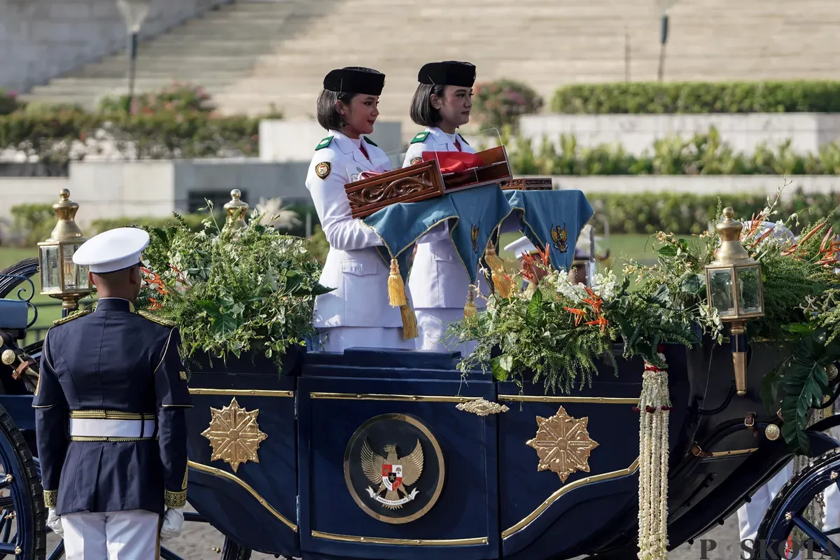 Purna Paskibraka Duta Pancasila 2024, Kirana Ashawidya Baskara dan Ni Komang Tri Setia membawa baki Bendera Pusaka Merah Putih dan Teks Proklamasi saat menaiki Kereta Kencana Garuda Prabayeksa pada Kirab Merah Putih HUT ke-80 Republik Indonesia di Monas, Jakarta, Minggu, 17 Agustus 2025 (Sumber: Poskota/Bilal Nugraha Ginanjar)