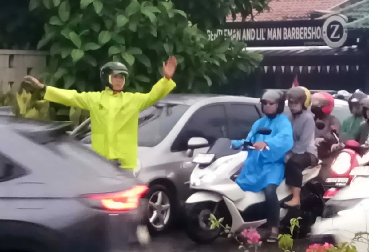 Seorang polisi mengenakan jas hujan mengatur arus lalu lintas di Jalan Raya Cinere, Depok, saat hujan deras yang menyebabkan kemacetan pada Selasa, 19 Agustus 2025). (Sumber: Poskota/Angga Pahlevi)