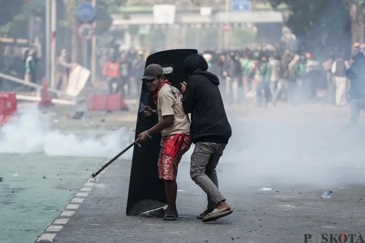 Dua massa aksi berlindung di balik tameng polisi saat demonstrasi di Mako Brimob Polda Metro Jaya, Kecamatan Senen, Jakarta Pusat, Jumat, 29 Agustus 2025. (Sumber: Poskota/Bilal Nugraha Ginanjar)