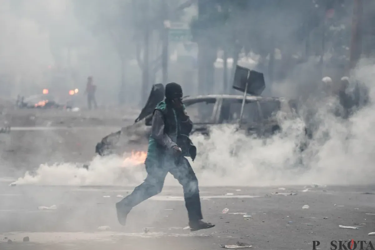 Seorang pengemudi ojol berada di tengah-tengah kepulan asap saat demonstrasi di Satuan Brimob Polda Metro Jaya, Kecamatan Senen, Jakarta Pusat, Jumat, 29 Agustus 2025. (Sumber: Poskota/Bilal Nugraha Ginanjar)