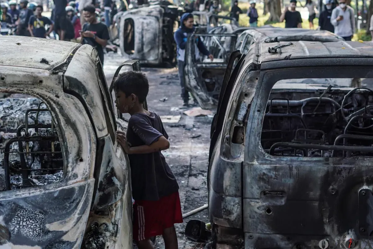 Seorang anak kecil melihat kendaraan roda empat yang terbakar saat demonstrasi di Mako Brimob Polda Metro Jaya, Kwitang, Jakarta Pusat, Jumat, 29 Agustus 2025. (Sumber: Poskota/Bilal Nugraha Ginanjar)